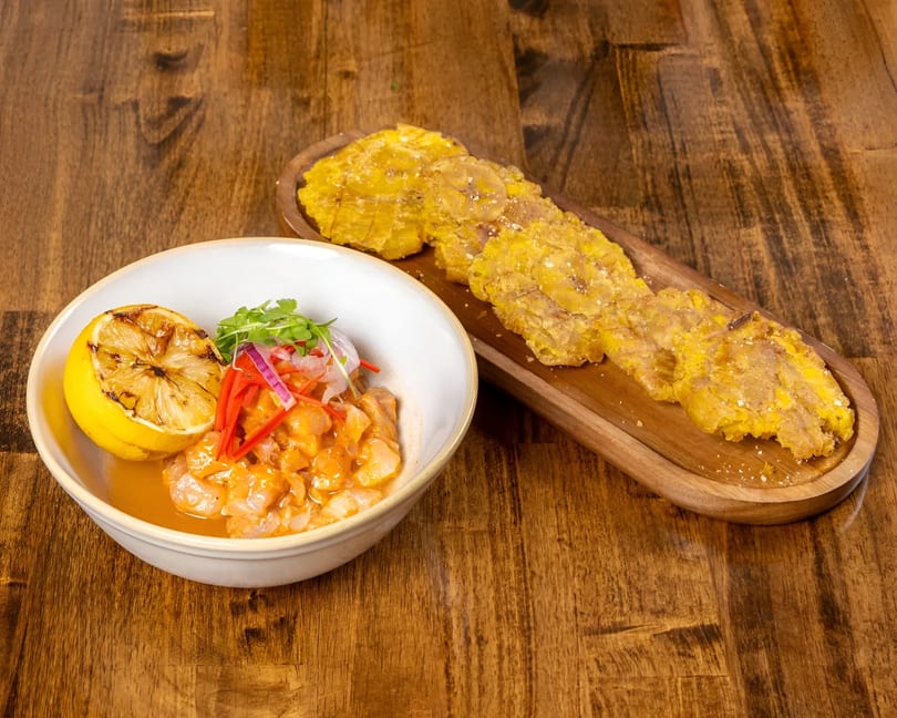 Ceviche with grilled lemon and plantain chips on a wooden table.