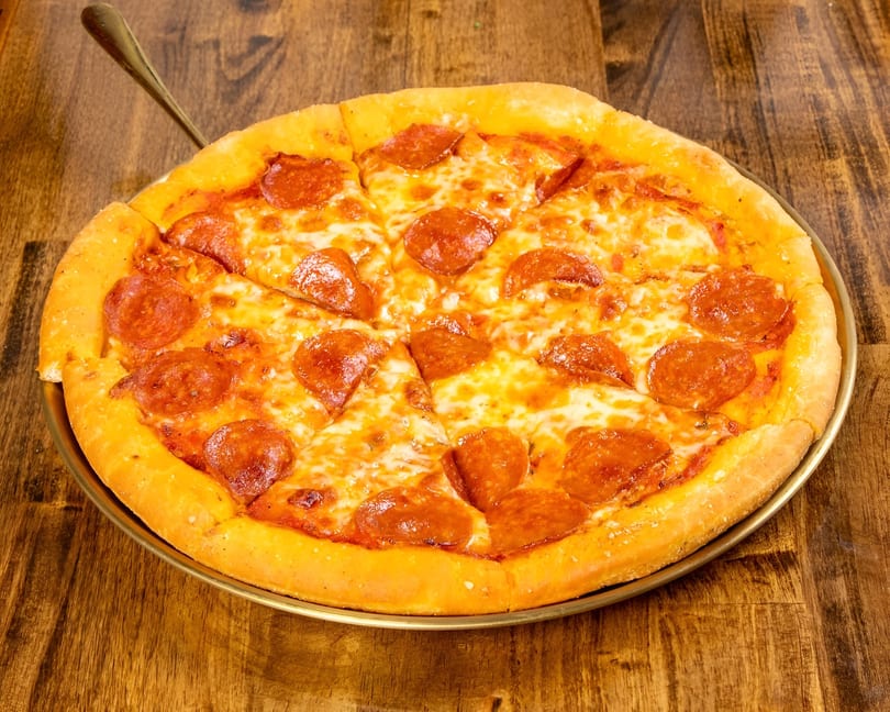 A whole pepperoni pizza with melted cheese and a thick crust, on a wooden table.